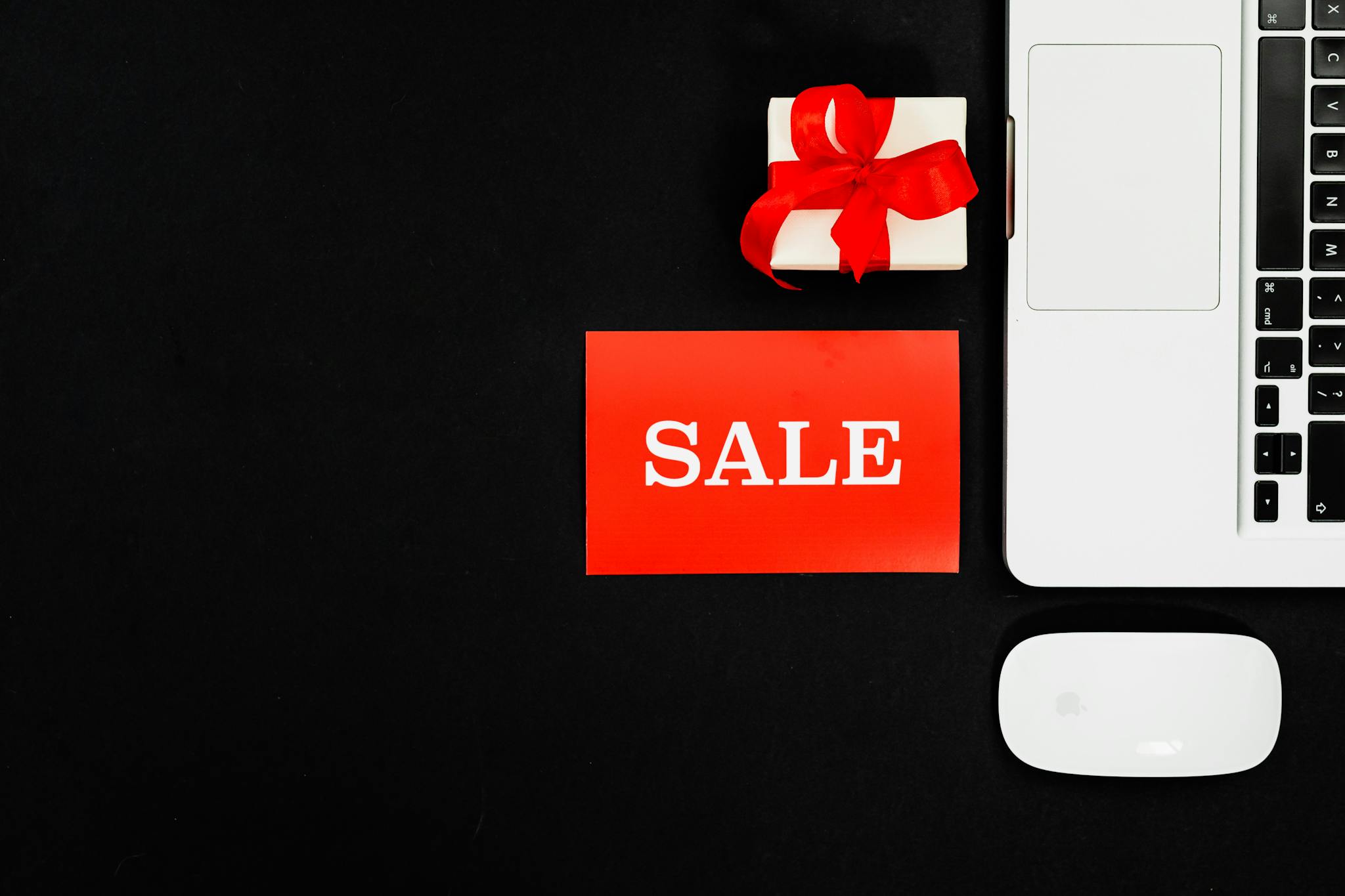 Flat lay of a laptop, gift box, and sale sign for online shopping promotion.